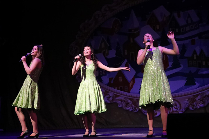 A trio of singing young women dressed in glittery green dresses
