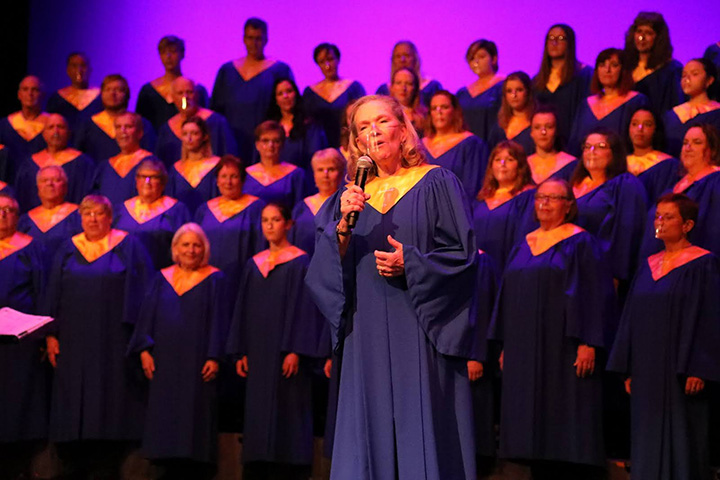 A choir dressed in blue choir robes with gold stoles, a soloist stands in the foreground