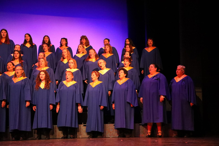 Adults dressed in blue choir robes with gold stoles sing.