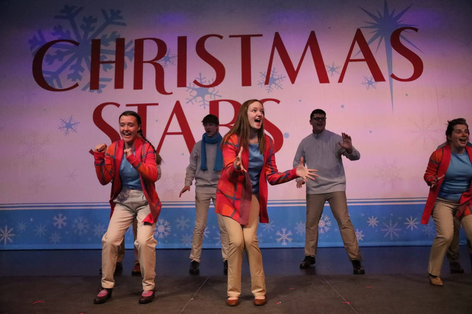 Two men and three women dance in front of a Christmas Stars drop.