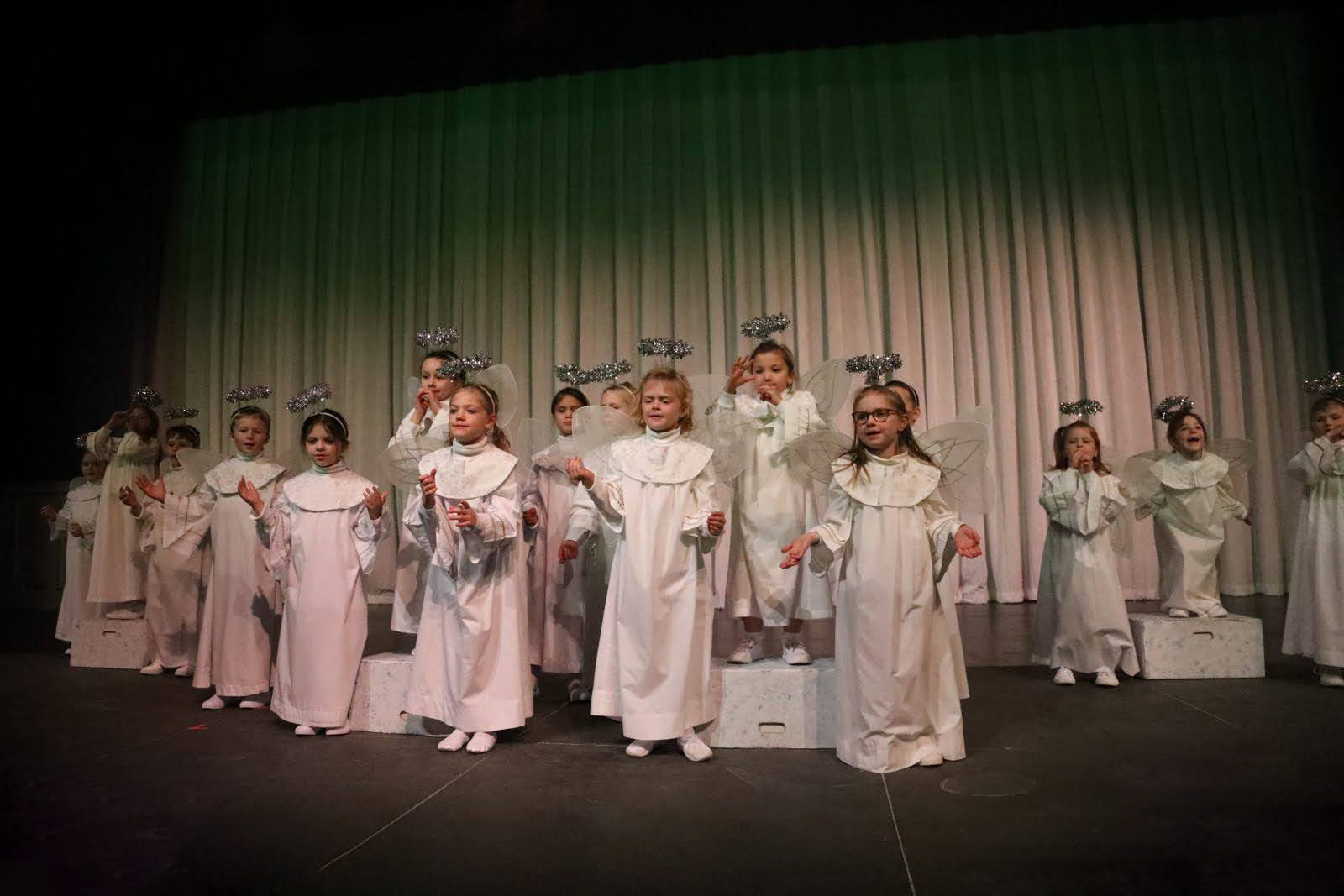 Young children dressed in angel robes with halos and wings strike a pose.