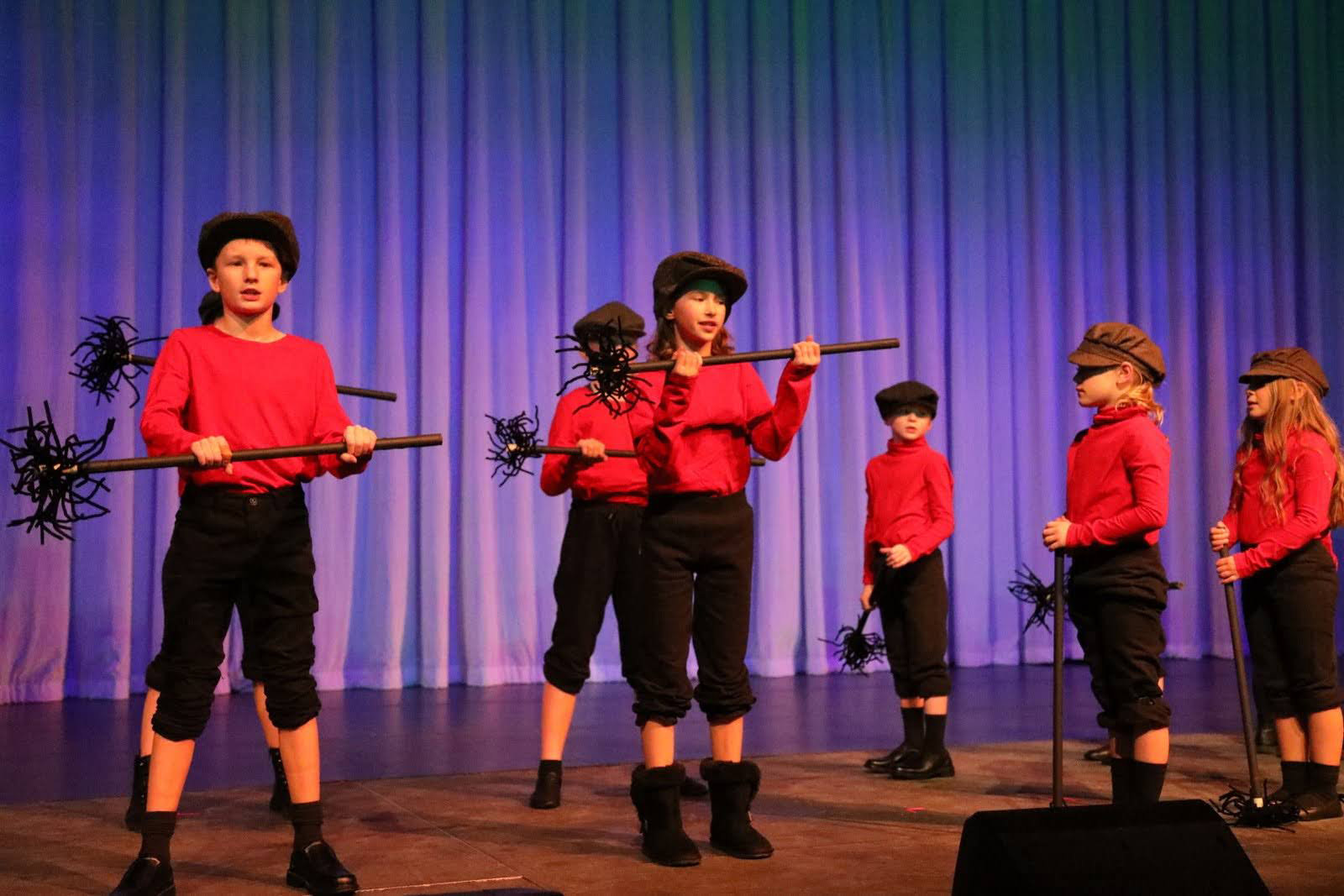 Children dressed as chimney sweeps dance with chimney brushes.